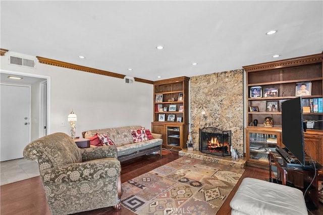 living room featuring built in features, crown molding, a fireplace, and wood-type flooring