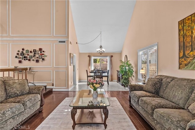 living room with high vaulted ceiling, an inviting chandelier, and dark hardwood / wood-style floors