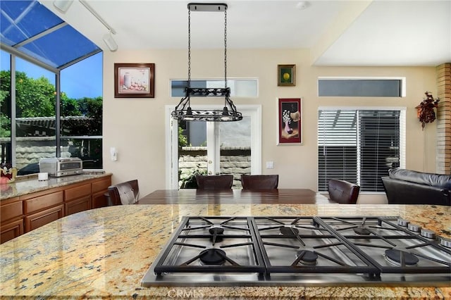 kitchen with gas cooktop, hanging light fixtures, rail lighting, and light stone countertops