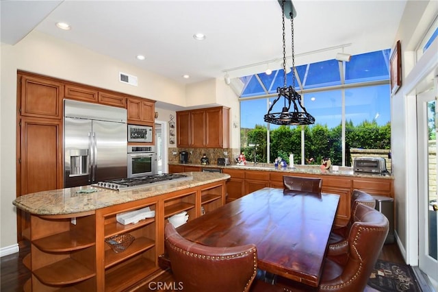 kitchen with a center island, decorative light fixtures, built in appliances, tasteful backsplash, and light stone counters