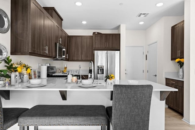 kitchen with kitchen peninsula, dark brown cabinetry, a kitchen bar, and appliances with stainless steel finishes