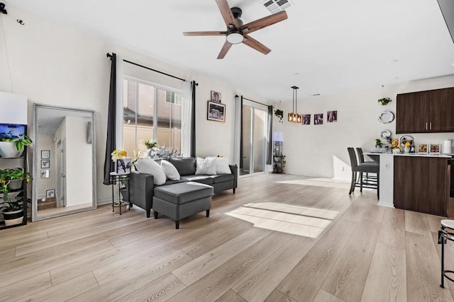 living room with ceiling fan with notable chandelier and light hardwood / wood-style floors