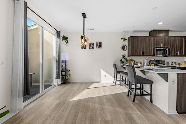 kitchen featuring appliances with stainless steel finishes, light hardwood / wood-style floors, kitchen peninsula, a breakfast bar, and dark brown cabinets