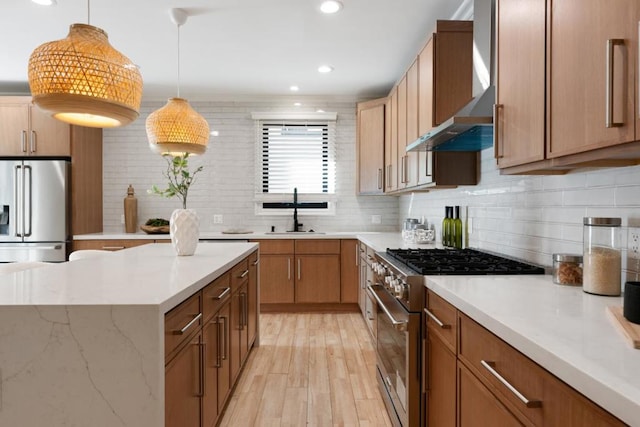 kitchen featuring pendant lighting, wall chimney range hood, sink, backsplash, and premium appliances