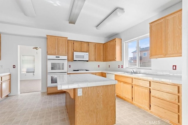 kitchen with a kitchen breakfast bar, light brown cabinetry, sink, white appliances, and a kitchen island