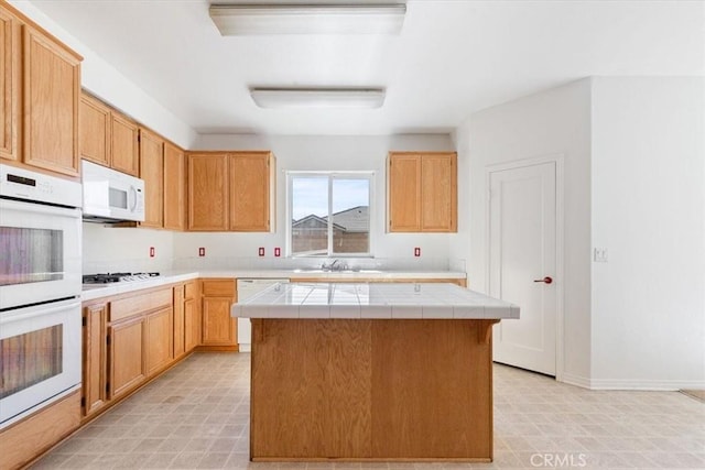 kitchen with white appliances, tile counters, sink, a kitchen island, and light brown cabinets