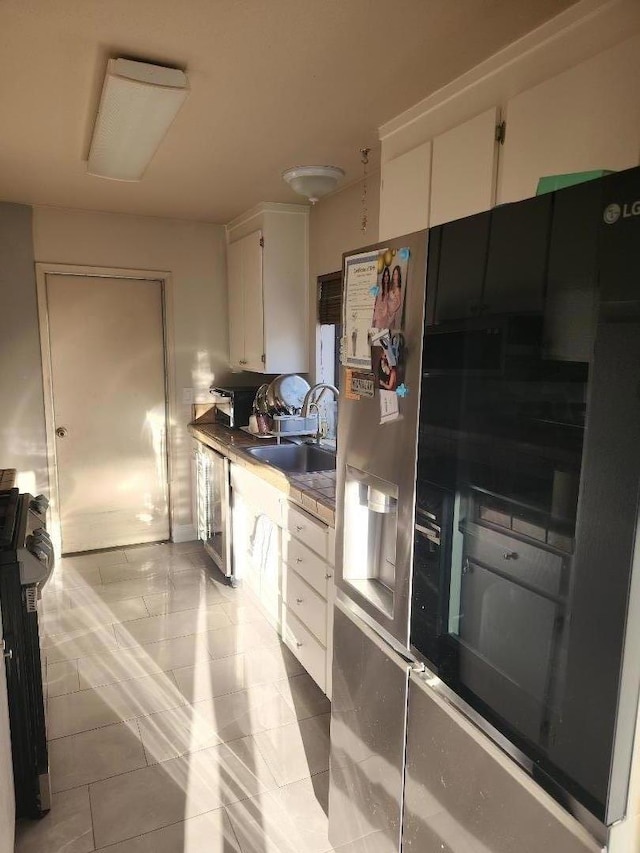 kitchen with range, stainless steel refrigerator with ice dispenser, white cabinetry, sink, and light tile patterned floors