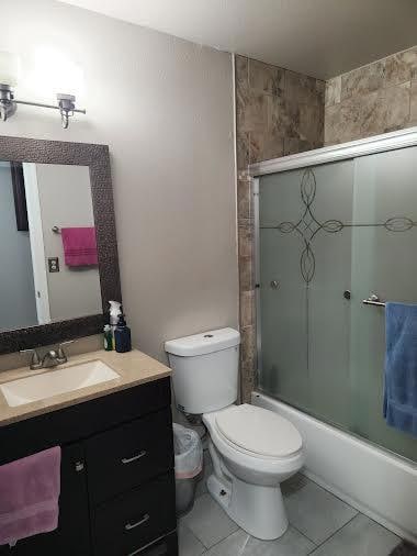 full bathroom with combined bath / shower with glass door, toilet, tile patterned flooring, and vanity