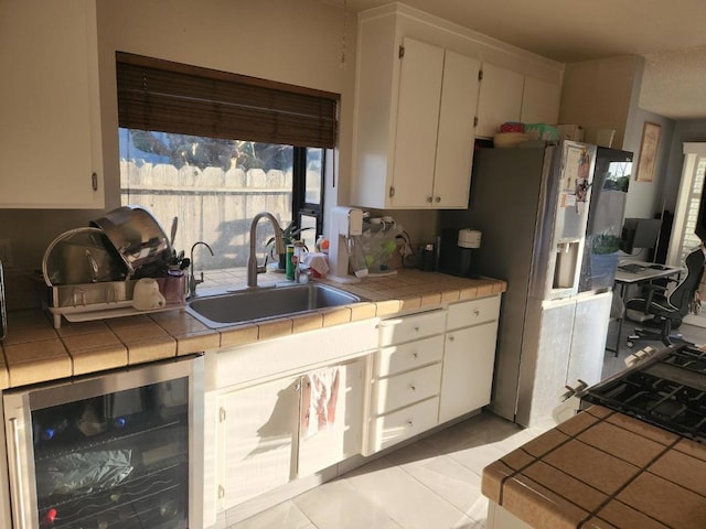 kitchen with sink, white cabinetry, light tile patterned floors, beverage cooler, and tile counters