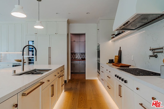 kitchen featuring sink, premium range hood, white cabinets, decorative light fixtures, and light hardwood / wood-style floors