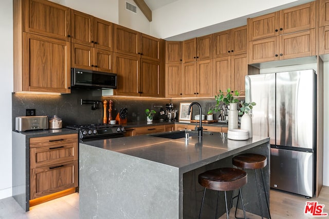 kitchen with sink, light wood-type flooring, a kitchen island with sink, black appliances, and a breakfast bar area