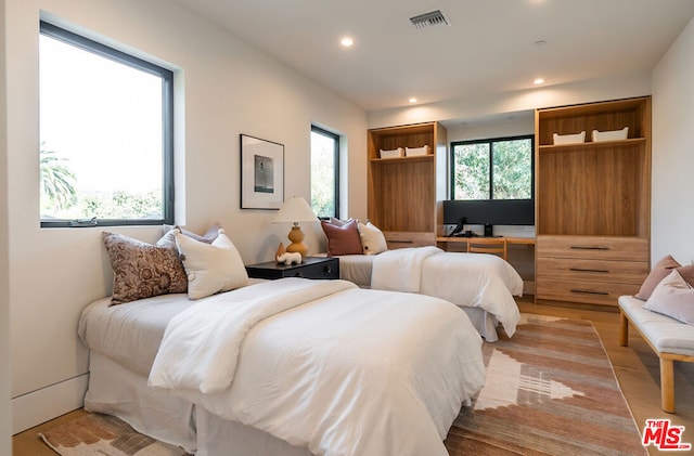 bedroom with light wood-type flooring, built in desk, and multiple windows