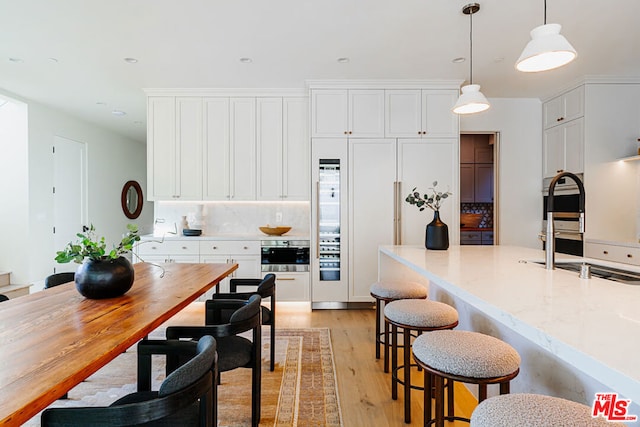 kitchen with light stone countertops, white cabinets, light wood-type flooring, pendant lighting, and backsplash