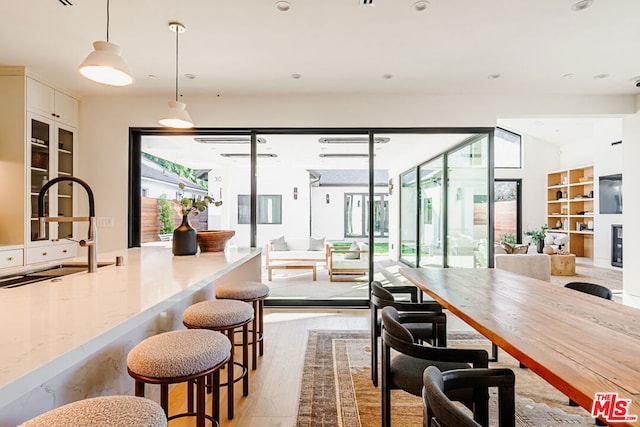 interior space featuring light stone countertops, decorative light fixtures, white cabinetry, sink, and light hardwood / wood-style flooring