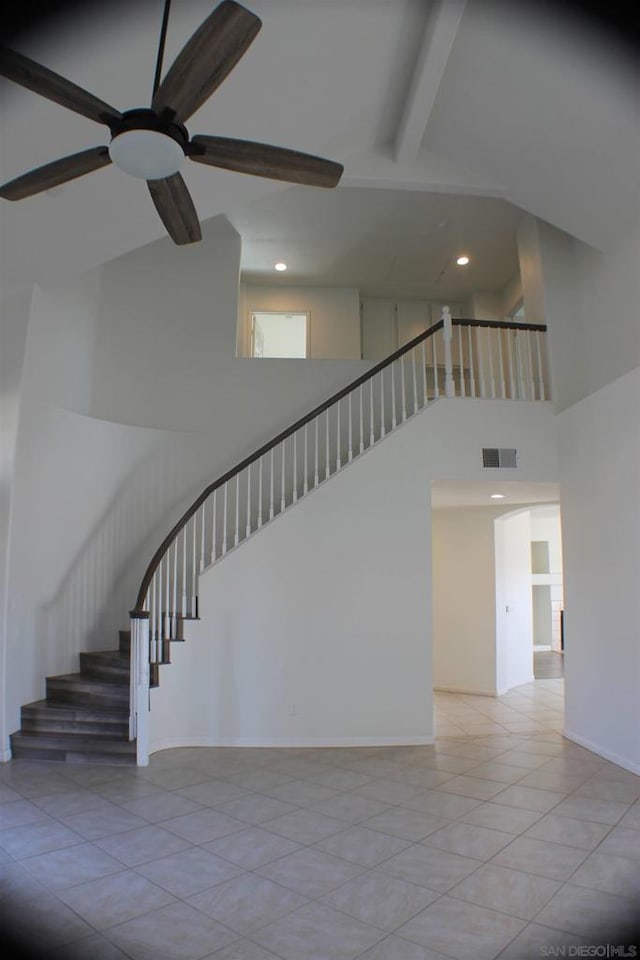 staircase with ceiling fan, tile patterned floors, beamed ceiling, and a towering ceiling