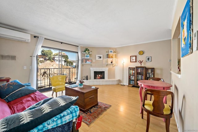 living room featuring crown molding, light hardwood / wood-style floors, a fireplace, a textured ceiling, and an AC wall unit