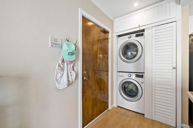 clothes washing area with stacked washer and clothes dryer, ornamental molding, and light wood-type flooring