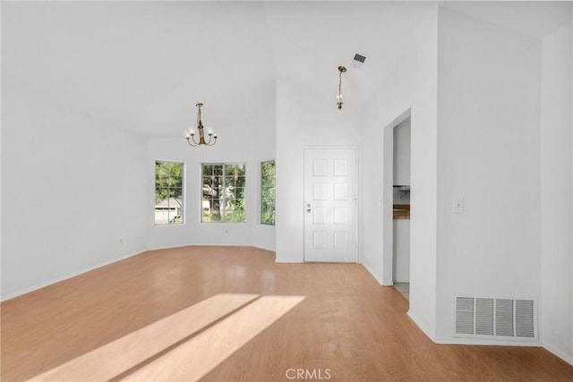 spare room featuring light wood-type flooring, a high ceiling, and an inviting chandelier