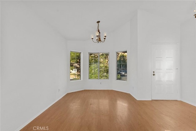 unfurnished dining area featuring light wood-type flooring, a chandelier, and lofted ceiling