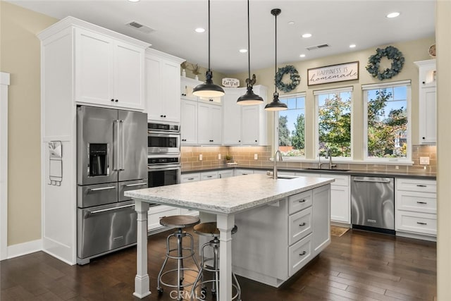 kitchen with a center island with sink, white cabinets, hanging light fixtures, and stainless steel appliances