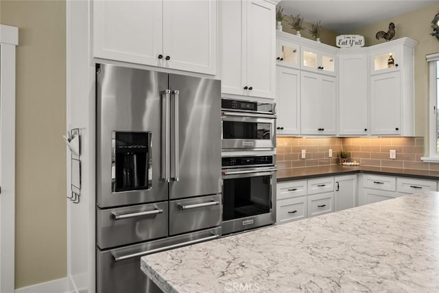 kitchen featuring stainless steel appliances, white cabinetry, dark stone counters, and decorative backsplash