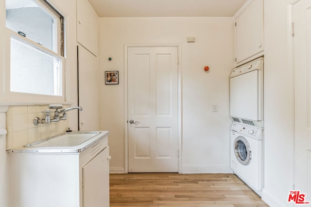 laundry room with sink, light hardwood / wood-style floors, and stacked washer / dryer