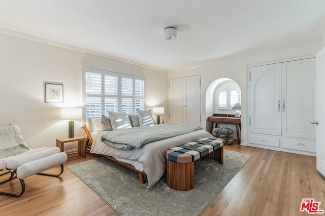 bedroom featuring ornamental molding, two closets, and light hardwood / wood-style flooring