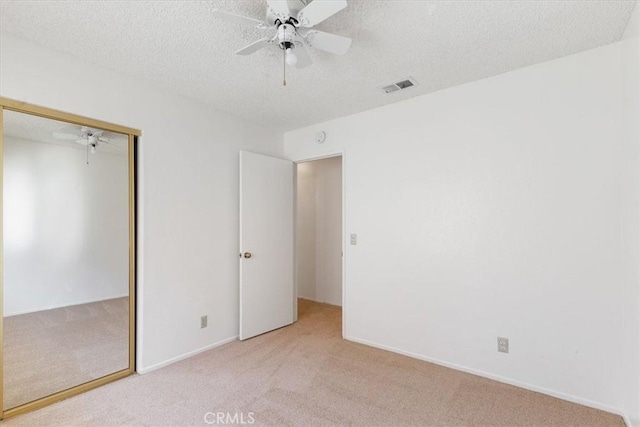 unfurnished bedroom featuring a closet, ceiling fan, a textured ceiling, and light carpet