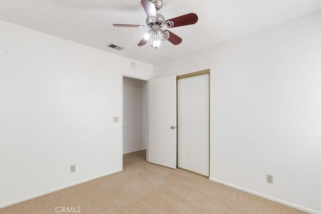 unfurnished bedroom with a closet, ceiling fan, a textured ceiling, and light carpet