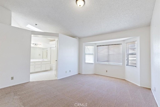 empty room with light carpet, a textured ceiling, and vaulted ceiling