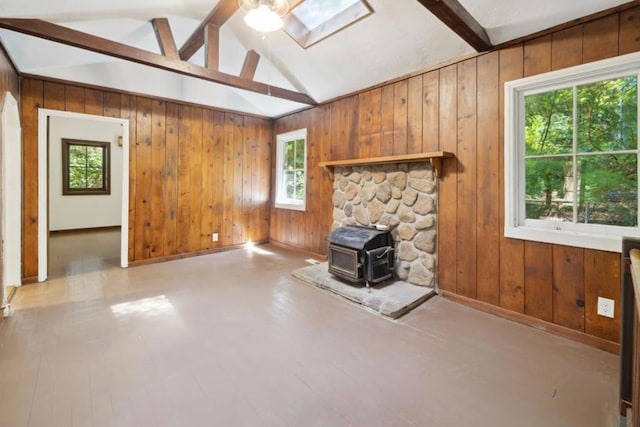 unfurnished living room featuring ceiling fan, wood walls, vaulted ceiling with skylight, and a wood stove