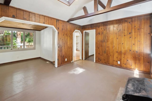 empty room with vaulted ceiling with beams, wooden walls, and concrete flooring