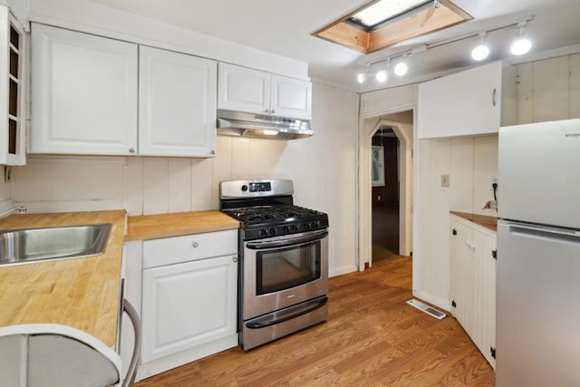 kitchen featuring stainless steel gas range oven, white cabinets, refrigerator, and wooden counters