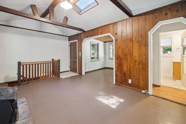 additional living space featuring concrete flooring, vaulted ceiling with skylight, and wood walls