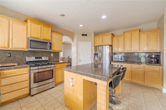 kitchen featuring light brown cabinets, appliances with stainless steel finishes, backsplash, light tile patterned floors, and a kitchen island