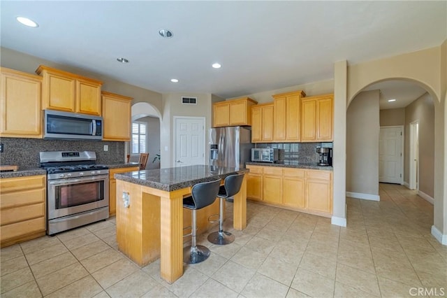 kitchen with light brown cabinets, appliances with stainless steel finishes, a center island, and a breakfast bar area