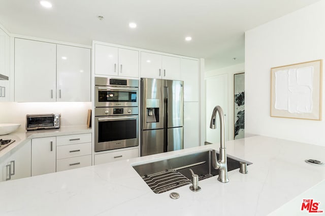 kitchen featuring light stone countertops, white cabinetry, appliances with stainless steel finishes, and sink