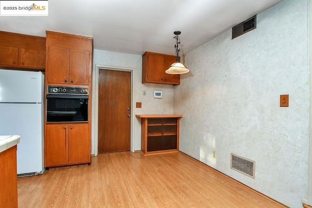 kitchen with decorative light fixtures, light hardwood / wood-style floors, oven, and white fridge