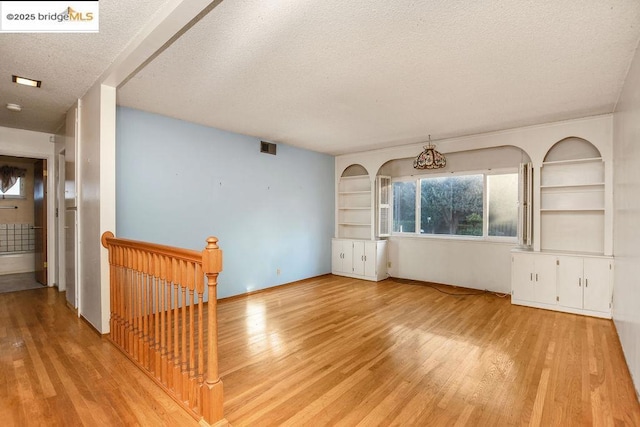 interior space with light hardwood / wood-style floors, a textured ceiling, and built in features