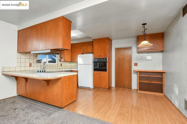 kitchen with black appliances, tile counters, light hardwood / wood-style flooring, kitchen peninsula, and pendant lighting