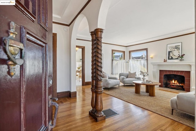 living room with light hardwood / wood-style flooring, ornate columns, crown molding, and a tiled fireplace