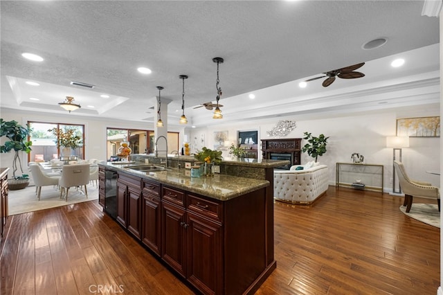 kitchen with a kitchen island with sink, sink, decorative light fixtures, a raised ceiling, and dark wood-type flooring