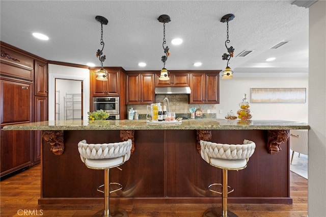 kitchen featuring a large island, pendant lighting, dark wood-type flooring, and a breakfast bar