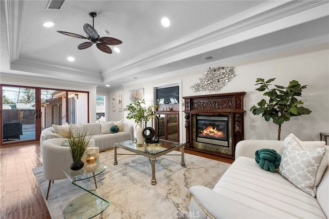 living room with a high end fireplace, hardwood / wood-style flooring, ornamental molding, ceiling fan, and a tray ceiling