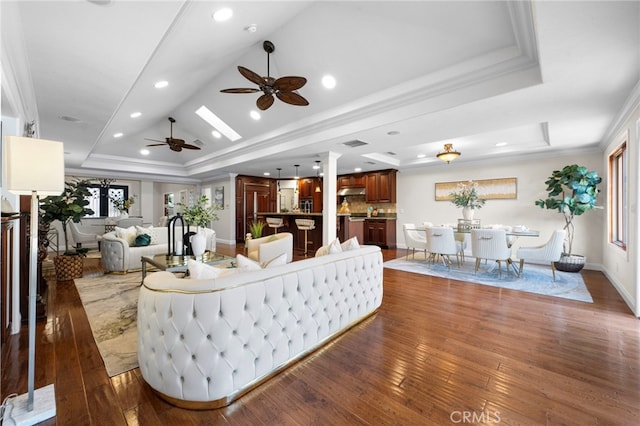 living room featuring ceiling fan, dark hardwood / wood-style flooring, a tray ceiling, and ornamental molding