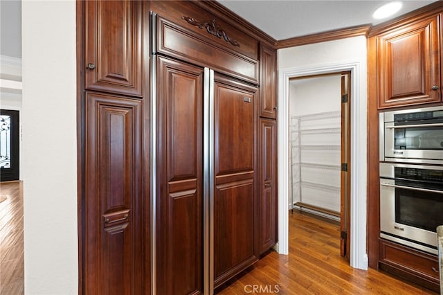 kitchen with dark wood-type flooring, double oven, and ornamental molding