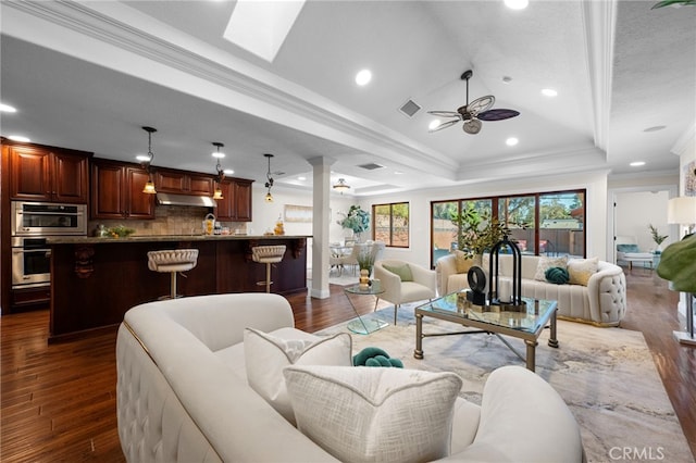 living room featuring a skylight, dark hardwood / wood-style flooring, crown molding, and a raised ceiling