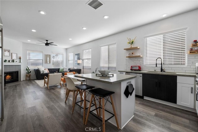 kitchen featuring visible vents, a tiled fireplace, a kitchen breakfast bar, a sink, and stainless steel dishwasher