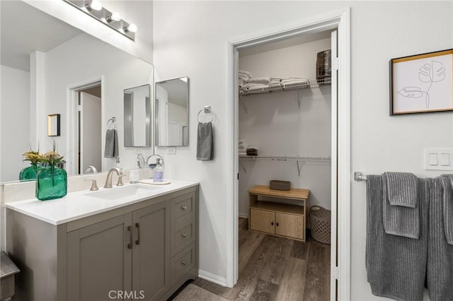 bathroom with a walk in closet, vanity, baseboards, and wood finished floors