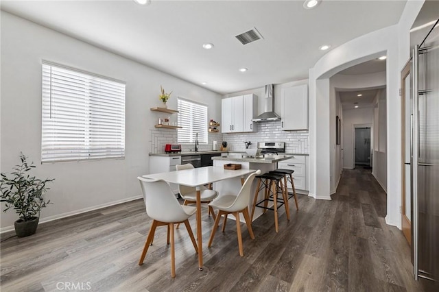 kitchen with wall chimney range hood, a kitchen island, visible vents, and decorative backsplash